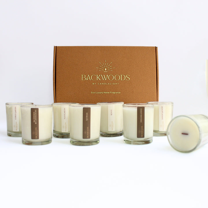 Complete Discovery Scent Set: eight 2.5 oz wooden wick votives lined up in front of a kraft Backwoods By Candlelight box with a gold foil logo
