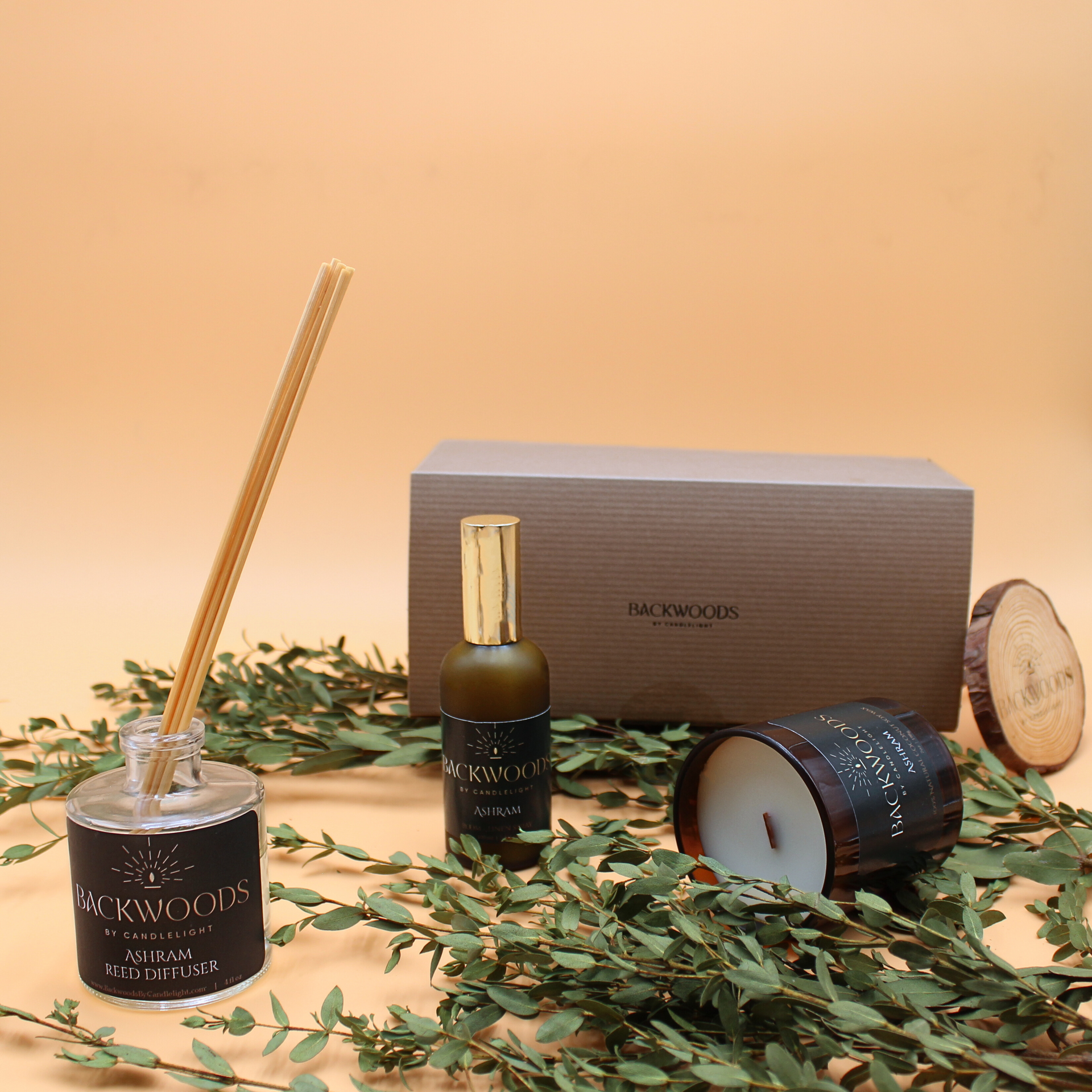 Backwoods diffuser, bottle, and candle on a beige background with green leaves. Candle gift set. 
