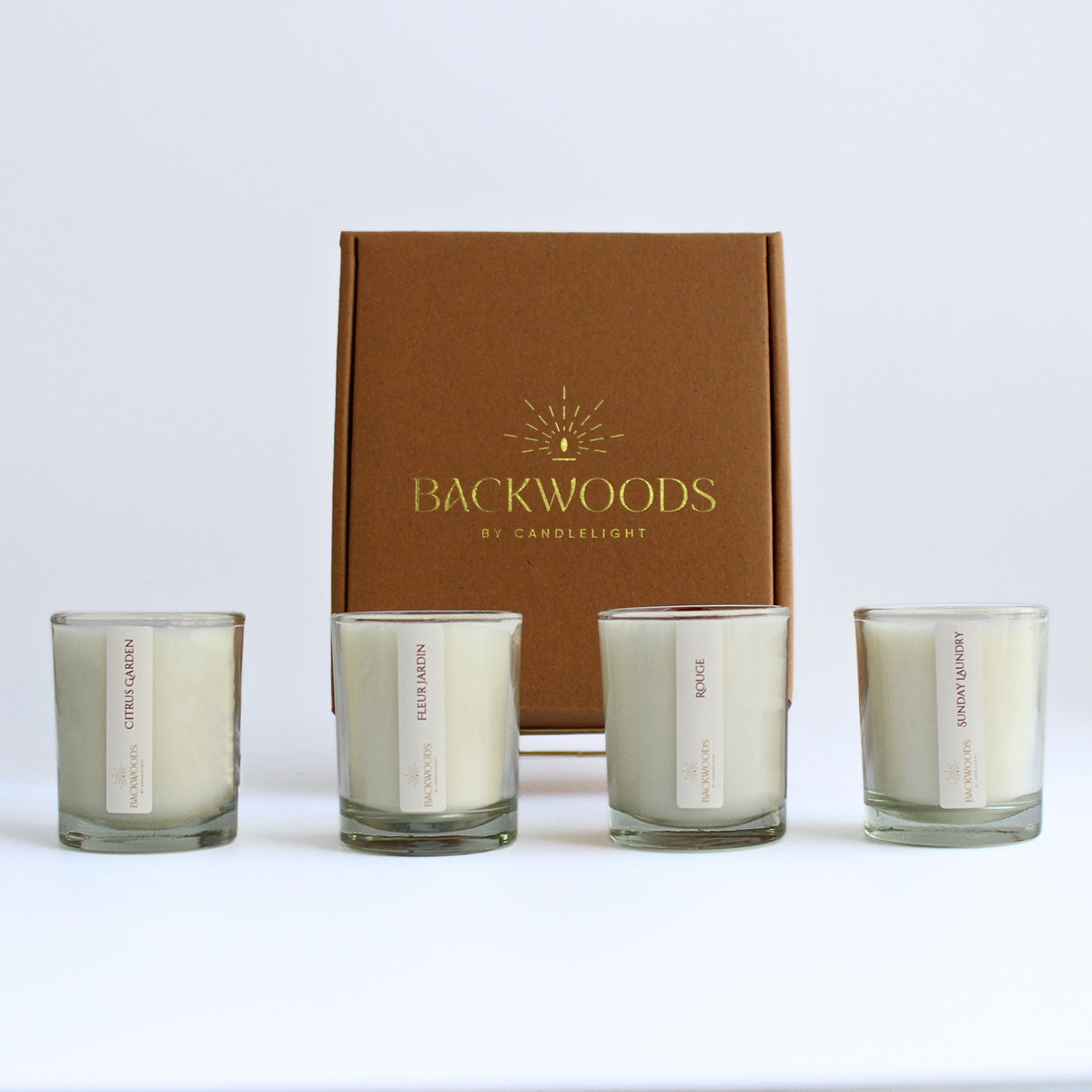 Light & Fresh Discovery Scent Set: four 2.5 oz wooden wick votives in front of a kraft Backwoods By Candlelight box with a gold foil logo