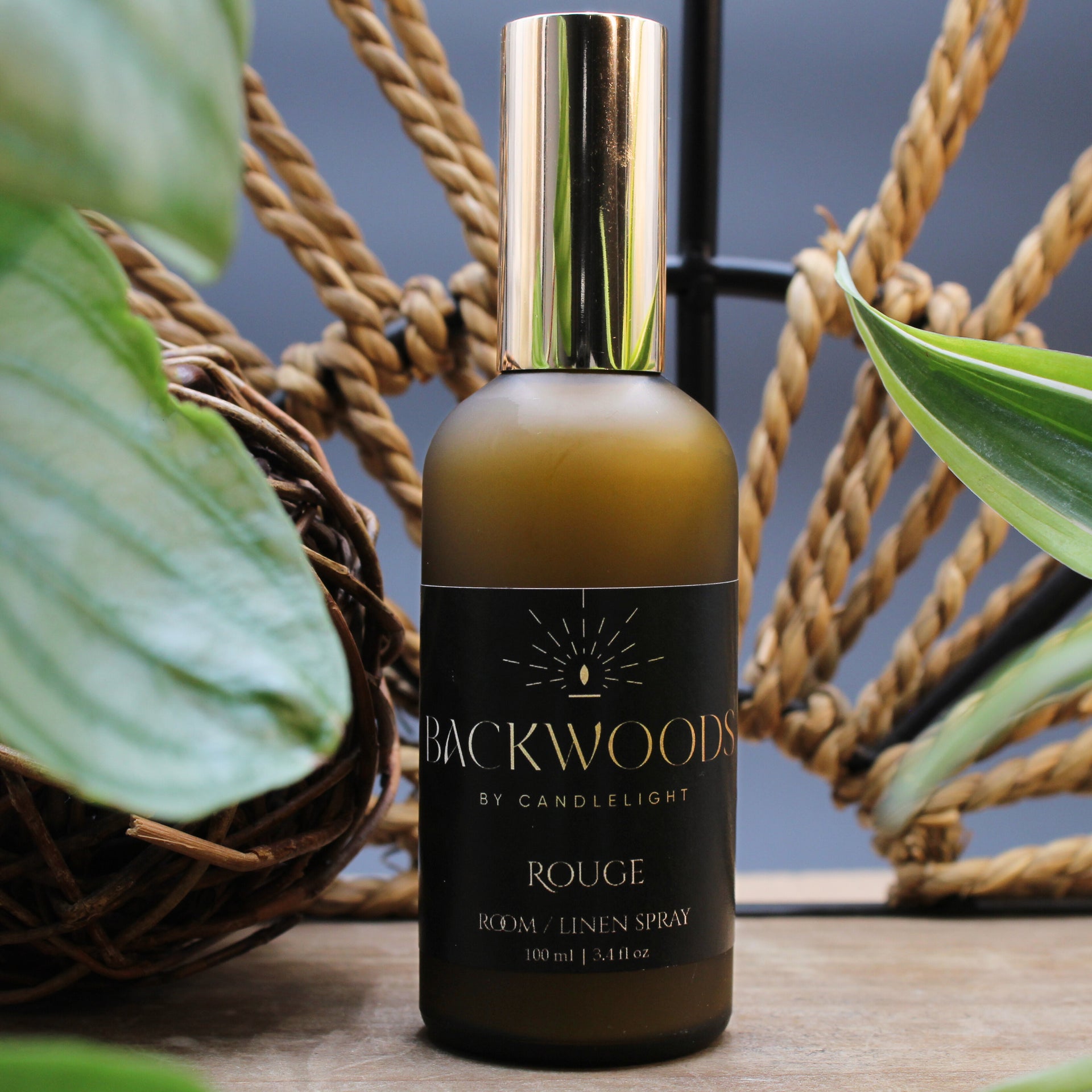 Brown spray bottle with gold cap labeled 'Backwoods by Candlelight Rouge' on a white background