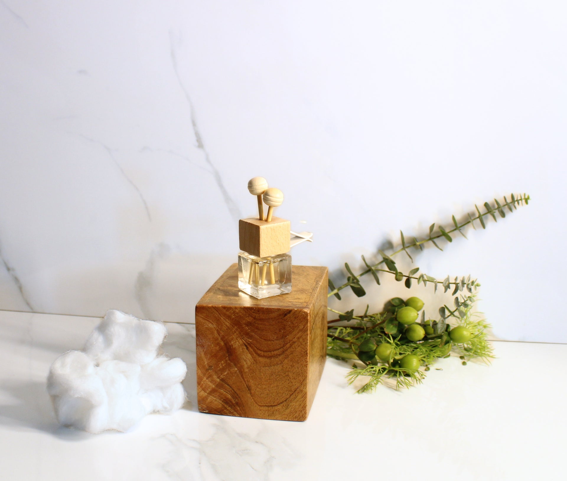 Clear car diffuser bottle with wooden top and two spherical objects on a white background