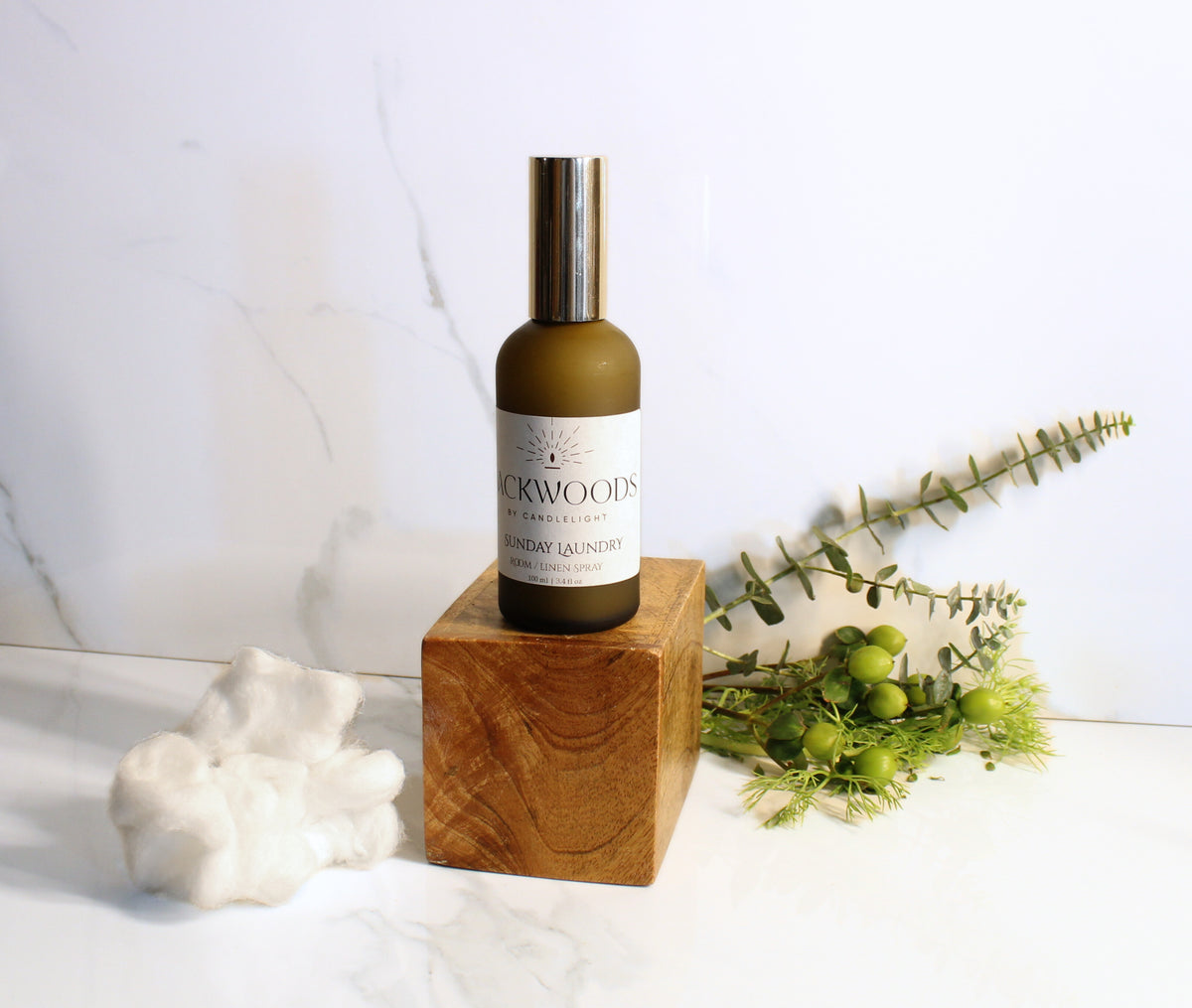 Bottle of 'Backwoods' product on a wooden block with greenery on a white background