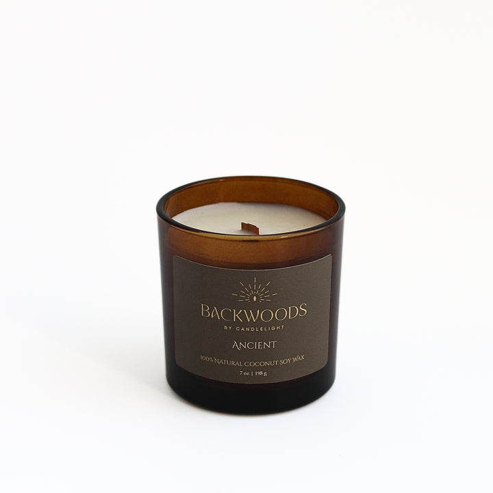 Ancient 7 oz wooden wick candle in an amber glass jar with an olive and gold label, on a white background